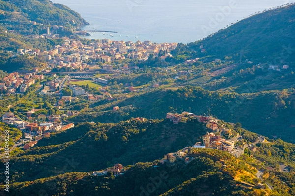 Fototapeta Colorful traditional houses with red roofs on Mediterranean sea shore on sunset, Liguria, Italy. Colors of amazing little Italian village in mountains covered by forests. Aerial nature travel view.