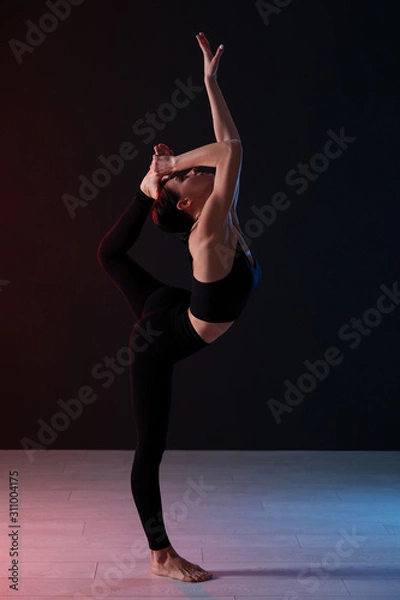 Fototapeta Young professional acrobat exercising in dark studio