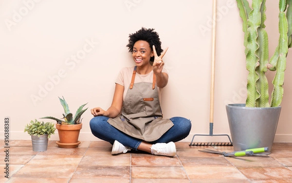 Fototapeta Gardener woman sitting on the floor smiling and showing victory sign