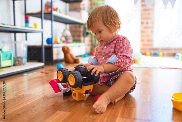 Fototapeta Adorable toddler playing with tractor around lots of toys at kindergarten