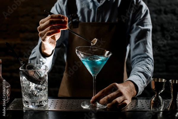 Fototapeta Male bartender deacorating a blue alcoholic cocktail in a martini glass with a spikelet