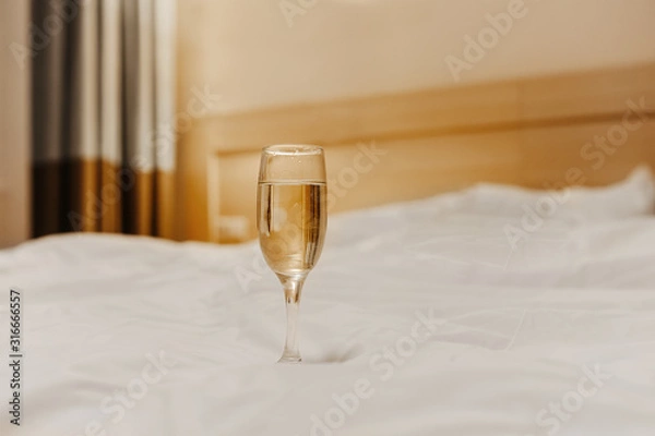 Fototapeta lonely glass goblet with a light drink on a pure white crumpled bed