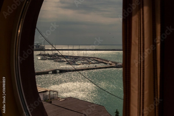 Fototapeta Room with a round window view over the docks with small boats on the coast of the Black Sea.