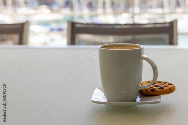 Fototapeta A cup of cappuccino cofee with cookie on a saucer. Copy space. Light background