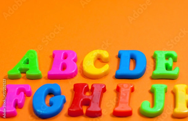 Fototapeta Plastic color letters on a bright contrasting orange background, multicolored alphabet with copy space