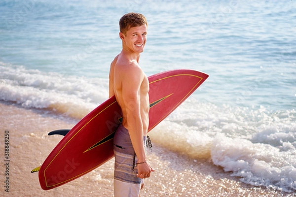 Fototapeta Hobby and vacation. Holiday on the beach. Young man carrying surf board.