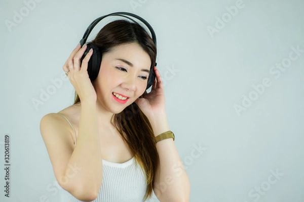 Obraz Portrait of beautiful asian woman with headphones listening to music.  happy, smiling / Caucasian female model isolated on white background.