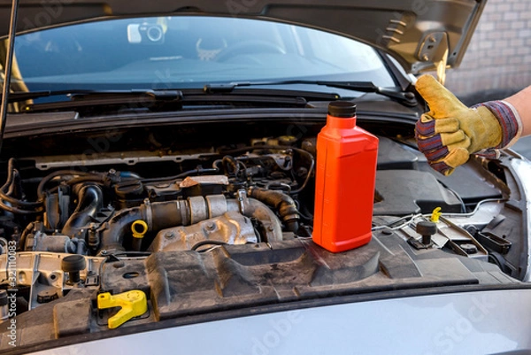 Fototapeta Oil change concept. Male hand in glove with oil bottle and car engine close up