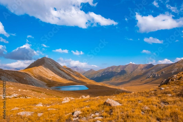 Fototapeta Mountain moraine lake in autumn with blue cloudy sky. Beautiful scenic view. Tranquil background, sunlight. Idyllic scenery. Beautiful alpine landscape. Mountain hiking.