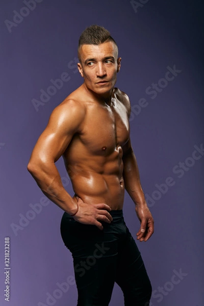 Fototapeta pleasant well-built man with hands on the hips showing his body after long effective training, close up portrait, isolated blue background, studio shot,