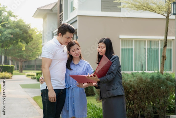 Fototapeta Asian woman Real estate broker agent showing a house detail in her file to the young Asian couple lover looking and interest to buy it. Buying a new house..