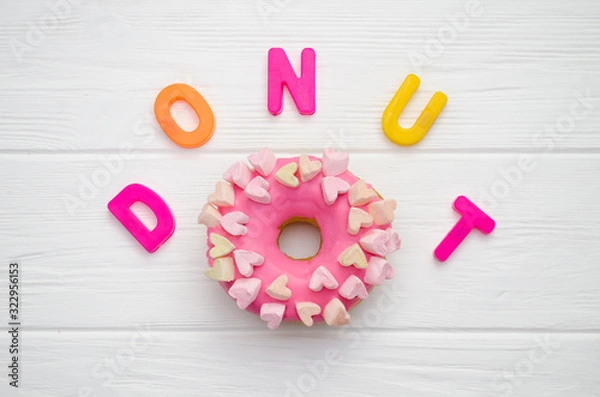 Fototapeta Sweet pink donut with icing and decoration with hearts on a white wooden background and with text letters