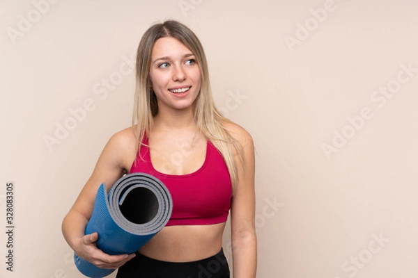 Fototapeta Young sport blonde woman over isolated background with a mat and smiling