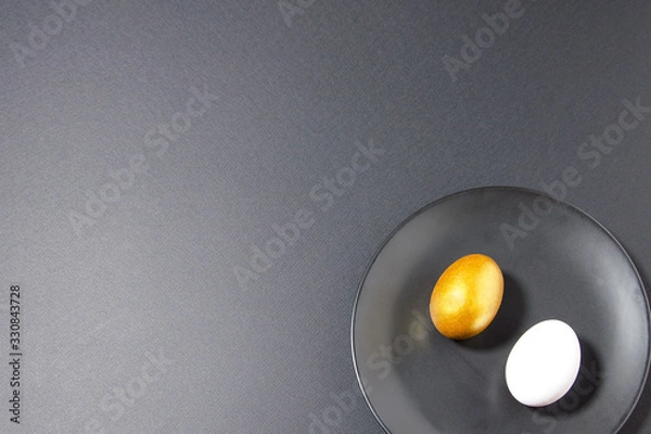 Fototapeta Easter attributes golden and white eggs lie on a black plate and on a black background. trend black monochrome