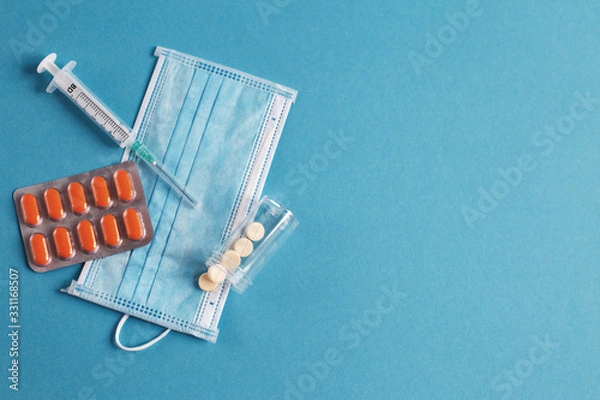 Fototapeta medical mask, syringe, tablets and vials with medicine on the blue background. Coronavirus, flu, disease concept.