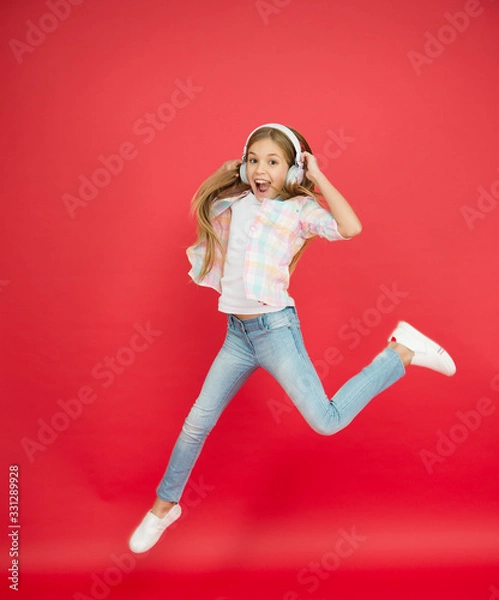 Fototapeta reach her dream. fly up in air. achievement. excited small girl wear headphones. show dance move. childhood happiness. happy kid listen music. child having fun. Little girl in earphones