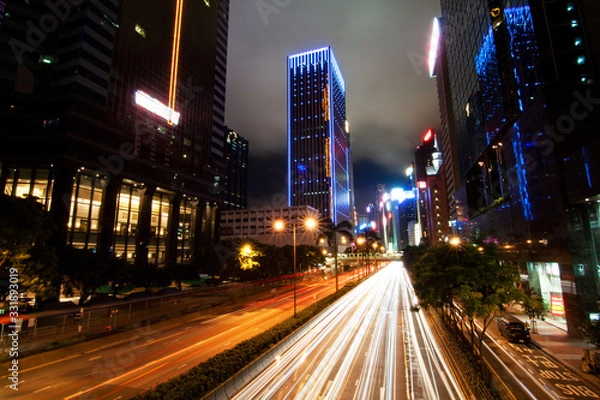 Fototapeta Long exposure shot with trailing lights of busy traffic at night in Hong Kong with lighted skyscrapers in the background