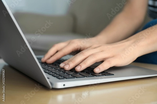 Fototapeta Woman working on modern laptop at wooden table indoors, closeup