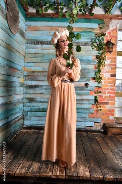 Fototapeta spring girl in a beige dress in a wreath of flowers against a blue wall