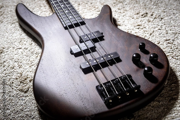 Obraz Bass electric guitar with four strings. Popular rock musical instrument. Close view of brown bass on carpet.