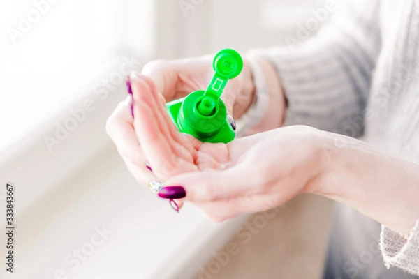 Fototapeta Girl disinfects hands with an antiseptic in a green bottle