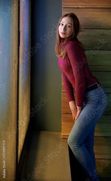 Fototapeta Photo of a cute teen girl one night in a window-light of a building outdoors.