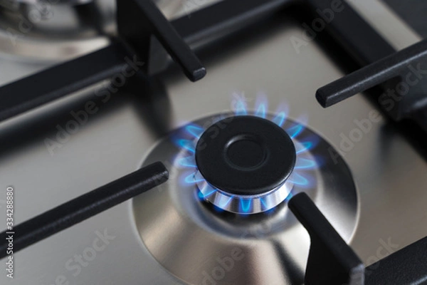 Fototapeta Closeup blue flame from a gas stove burner. Stainless steel kitchen surface with cast-iron grill.