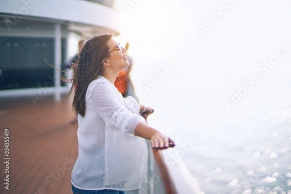 Fototapeta Young beautiful woman on vacation smiling happy and confident. Standing on a deck of ship with smile on face doing a cruise