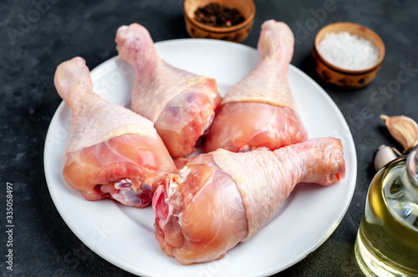 Fototapeta raw chicken legs with spices on a white plate with copy space for your text