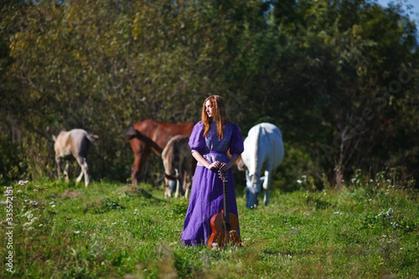 Fototapeta a girl with a guitar stands next to a horse and a foal