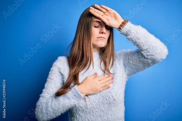 Fototapeta Young beautiful redhead woman wearing casual sweater over isolated blue background Touching forehead for illness and fever, flu and cold, virus sick