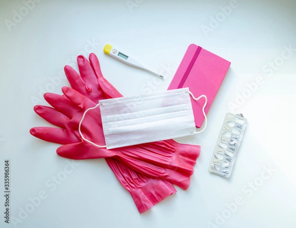 Fototapeta Quarantine set. Pink gloves and a notebook, mask, thermometer. pills on a white background. Flat lay