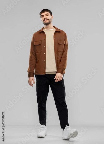 Fototapeta people concept - young man in brown jacket and black pants with mustaches over grey background