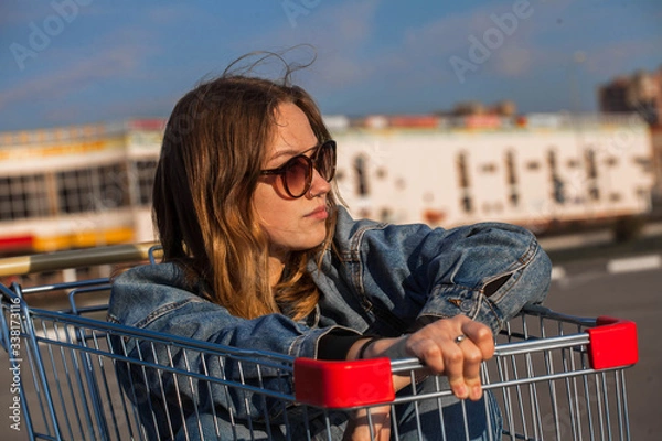 Fototapeta Girl sits in a grocery cart in the parking lot