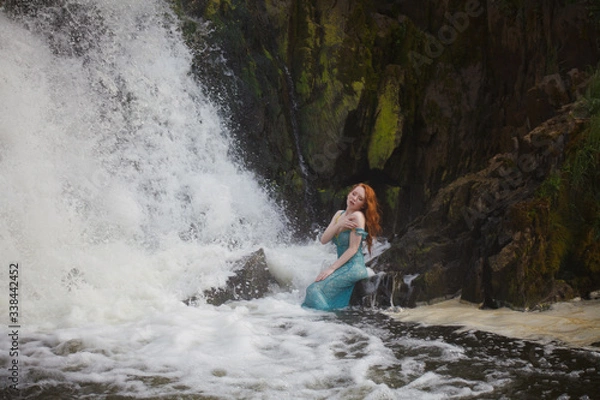 Fototapeta beautiful red-haired girl bathes in a stormy stream of a waterfall, hot summer