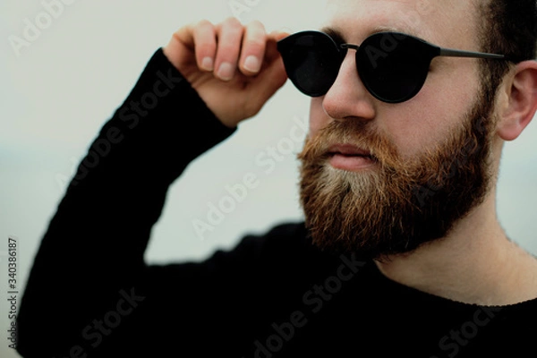 Fototapeta young man with beard and glasses on beach near sea