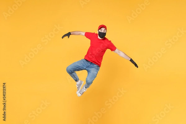 Fototapeta Fun jumping delivery man in red cap t-shirt uniform sterile face mask gloves isolated on yellow background studio Guy employee courier Service quarantine pandemic coronavirus virus 2019-ncov concept.