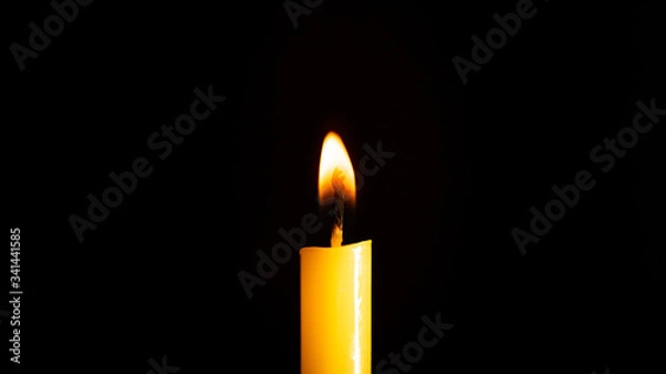 Fototapeta Close-up of a yellow candle illuminated in a black background.