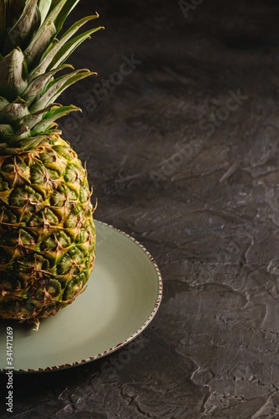 Fototapeta Fresh sweet pineapple in grey plate on dark black textured background, angle view, cropped