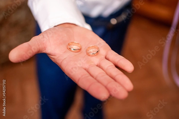 Fototapeta Groom holding golden wedding rings on the hand