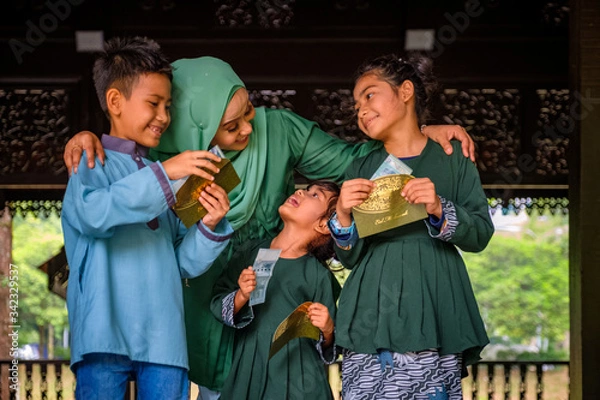 Fototapeta Happy children holding an envelope of pocket money or raya angpao from their mother during Eid al-Fitr celebration. Malaysian Family and Raya Concept.