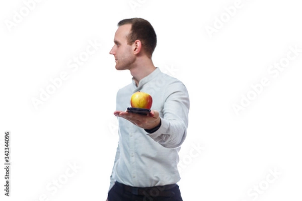 Fototapeta Caucasian male businessman holding a mobile phone in black and holding a red-yellow apple. He is wearing a shirt. Emotional portrait. Isolated on white background