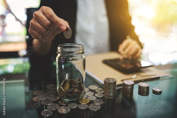 Obraz Closeup image of a businesswoman calculating, stacking and putting coins in a glass jar for saving money and financial concept