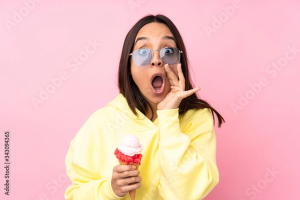 Fototapeta Young brunette girl holding a cornet ice cream over isolated pink background shouting and announcing something