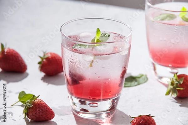 Fototapeta Glasses of strawberry water  with strawberries, ice and fresh mint leaves  on concrete background stone strong light with glass shadows. Copy space. Close up