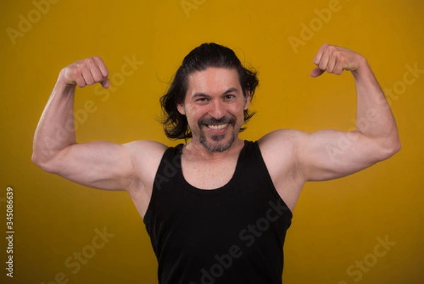 Fototapeta Male bodybuilder wearing dark tanktop on ripped muscular torso in studio shot ,