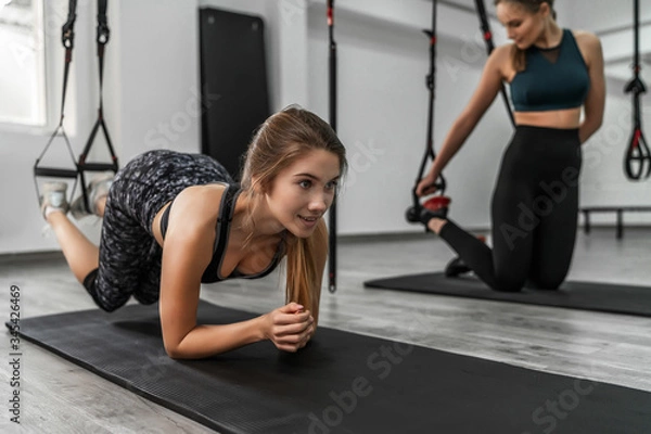 Fototapeta Healthy lifestyle. Portrait of young sportive girl doing plank with trx fitness straps in the gym