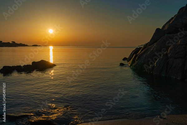 Fototapeta A view of the sea from the coast with the sunrise sun reflecting off and brightening the rocks with the colors of a wonderful sunrise on a summer day, in Sardinia Italy