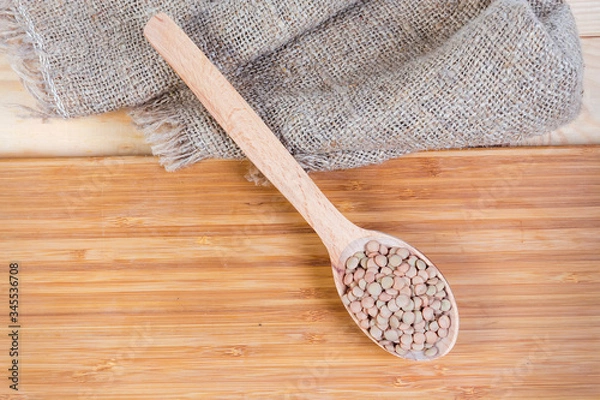 Fototapeta Uncooked brown lentil in wooden spoon on a wooden surface