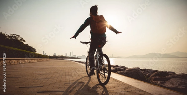 Fototapeta Female cyclist hands free cycling riding bike with arms outstretched in the coasts sunrise